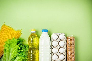 Essential fresh products lie on a green background. Eggs, greens, spaghetti, milk, cookies, sunflower oil. Food delivery covid-19 epidemic, Donation. top view. Copy space.