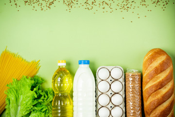 Essential fresh products lie on a green background. Eggs, greens, spaghetti, tomatoes, bread, milk, cookies, canned food. Food delivery covid-19 epidemic, Donation. top view. Copy space.