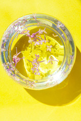 Lilac flowers float in the water. Purple and pink flowers in a glass vase. On a yellow  background