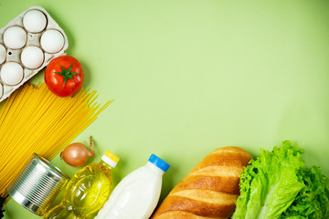 Essential fresh products lie on a green background. Eggs, greens, spaghetti, tomatoes, bread, milk, cookies, canned food. Food delivery covid-19 epidemic, Donation. top view. Copy space.