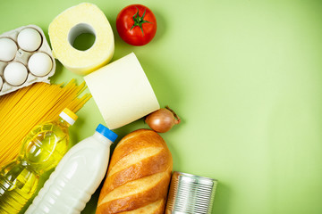 Essential fresh products lie on a green background. Eggs, greens, spaghetti, tomatoes, bread, milk, toilet paper, cookies, canned food. Food delivery covid-19 epidemic, Donation. top view. Copy space.