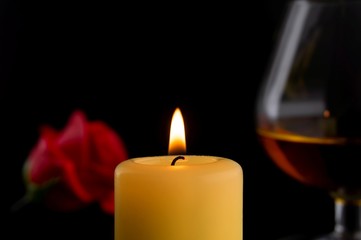 Burning yellow wax candle, glass and roses