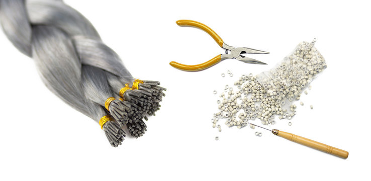 Women hair extension accessories and a fake brown har tail braided. Concept shot of a fake hair tail, pliers, tubes and a lacer, isolated on white background.