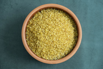 Raw bulgur in pot on stone, concrete background. Healthy, delicious and organic cereal. Flat lay, top view.