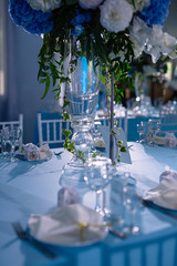 flowers stand in a vase on the festive table, the table is reserved, the table is covered with a blue tablecloth