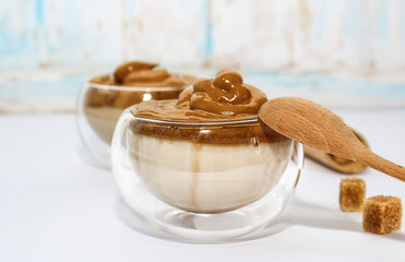 Dalgona coffee. Korean coffee in glasses cups and wooden spoon on white bacground. Drink with milk, sugar and coffee.