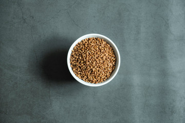 Buckwheat in white porcelain bowl on concrete, stone background. Healthy and organic cereal. Top view, flat lay.