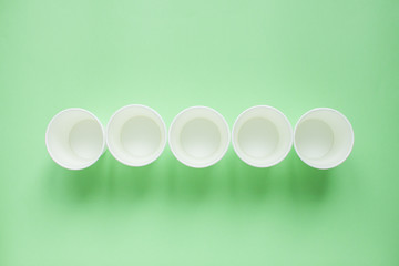 The layout on a green background from white paper disposable cups. Caring for the environment. Recycling garbage. Disposable tableware.
