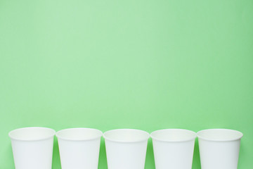 The layout on a green background from white paper disposable cups. Caring for the environment. Recycling garbage. Disposable tableware.