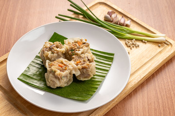 Asian Steam  Dumplings  or Dim Sum a Famous Chinese Food  with Pork and Shrimp on Banana Leaf and  Cutting Wood Board with Garlic, Spring Onion and Peppers.