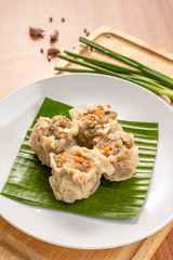 Close up Asian Steam  Dumplings  or Dim Sum a Famous Chinese Food  with Pork and Shrimp on Banana Leaf and  Cutting Wood Board with Garlic, Spring Onion and Peppers.