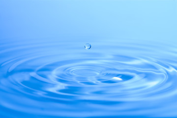 A drop of water over the water surface with circles of blue tones, close-up.