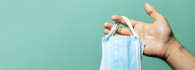 Fototapeta premium Close-up of male hand holding medical flu masks preventing coronavirus on background of cyan, aqua menthe color with shadows.