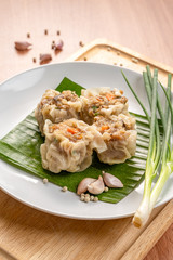 Close up Asian Steam  Dumplings  or Dim Sum a Famous Chinese Food  with Pork and Shrimp on Banana Leaf and  Cutting Wood Board with Garlic, Spring Onion and Peppers.