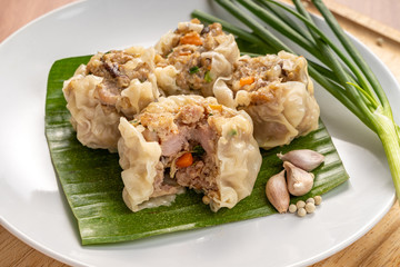 Close up Asian Steam  Dumplings  or Dim Sum a Famous Chinese Food  with Pork and Shrimp on Banana Leaf and  Cutting Wood Board with Garlic, Spring Onion and Peppers.