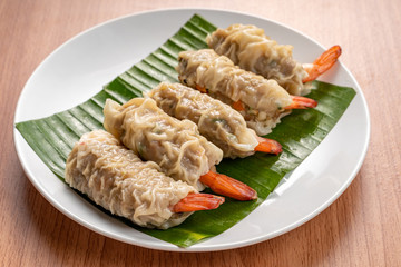 Close up Asian Steam  Dumplings  or Dim Sum a Famous Chinese Food  with Pork and Shrimp on Banana Leaf and White Dish on Wood Table.