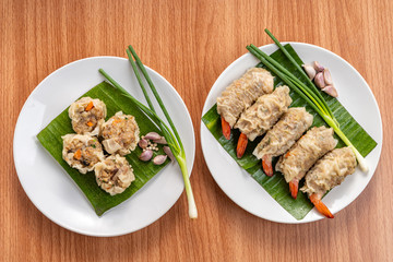 Close up Asian Steam  Dumplings  or Dim Sum a Famous Chinese Food  with Pork and Shrimp on Banana Leaf and White Dish on Wood Table with Spciy Ingredient.