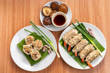 Close up Asian Steam  Dumplings  or Dim Sum a Famous Chinese Food  with Pork and Shrimp on Banana Leaf and White Dish on Wood Table with Spciy Ingredient.