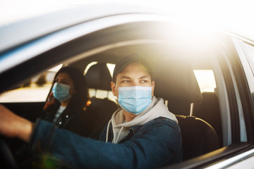 Man driving a car wearing sterile medical mask. Taxi driver with a passanger stuck in a traffic jam during coronavirus quarantine isolation in the city. Prevernt spread of covid-19 concept.