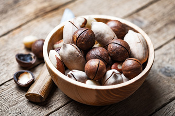 Dried mixed nuts in wooden bowl closeup. Macadamia, Pecan and Brazil nuts with knife on wooden table. Studio macro shoot.