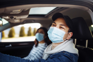 Man driving a car wearing sterile medical mask. Taxi driver with a passanger stuck in a traffic jam during coronavirus quarantine isolation in the city. Prevernt spread of covid-19 concept.