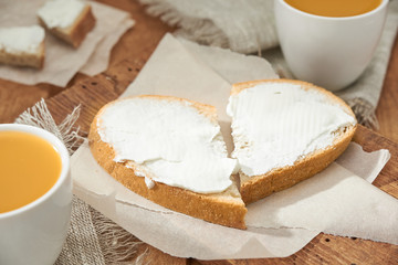 White bread slices with soft butter close up. Breakfast for two sandwiches laid out like a heart, two cups of juice on a wooden table.
