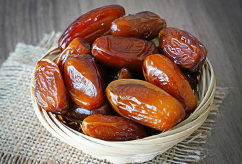 Fresh fruit dates in a basket bowl on a piece of sackcloth on walnut wooden table