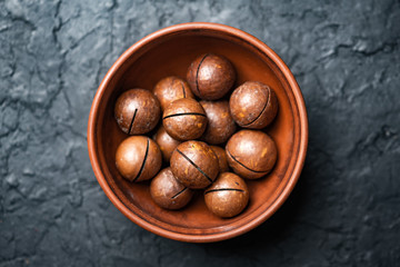 Dried organic Macadamia nuts in orange ceramic bowl closeup. Studio macro shoot. Black concrete background