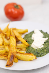 French fries and spinach on the plate with tomato in the blurred background