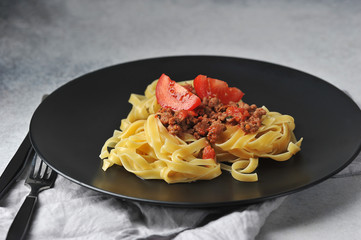 Pasta with bolognese sauce on a black plate.  A napkin and cutlery complete the composition. ...