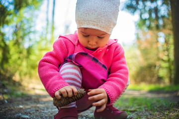 Adorable baby on forest path in nature. Portrait of 1 year old girl in woods with pine cone.