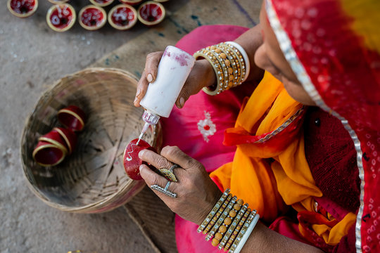 Indian woman in traditional costume decorating and painting a small clay bowl 