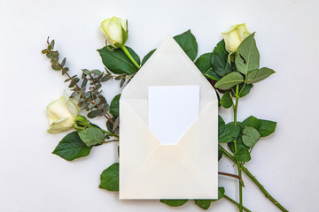 Flat lay composition with a white envelope, blank card and a rose flowers. Mockup for wedding or Valentine's day note. Top view.