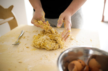 Staying at home with your family and preparing fresh home-made pasta (tagliatelle): mom mixing ingredients and kneading the dough on a wooden board.