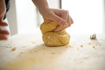 Staying at home with your family and preparing fresh home-made pasta (tagliatelle): mom kneading the dough on a wooden board.
