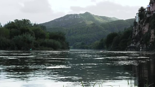 Ribera del r&iacute;o Ebro en la localidad de Miravet. La corriente pasa tranquilamente cruzando un paisaje de arboles y monta&ntilde;as en un d&iacute;a con alguna nube pasajera.