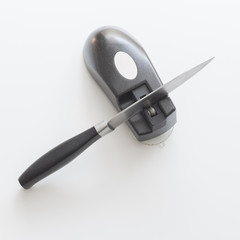 Knife and knife sharpener on a white surface. Kitchen tools isolated on white background.