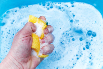 yellow sponge in hand on a blue background, soap foam