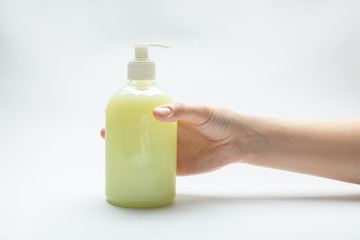 Female hand and bottle with dispenser with yellow liquid soap antiseptic standing on the table on a white background. Horizontal orientation.