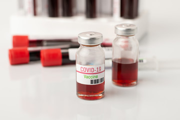 Bottles with coronavirus vaccine near blood test-tubes on doctor`s table