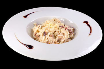 Tasty risotto with seafood in a white plate, isolated on black background