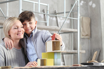 Happy mother and son playing building a house with construction models at interior site. House buy and building goal concept