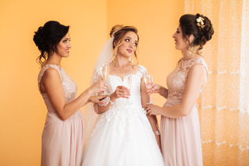 Bride with merry girlfriends at the wedding drink champagne from glasses. Bride and girlfriends hug in the room. Morning Bride and girlfriends.