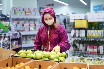 Fototapeta premium woman in protective mask and gloves buys fruit in a supermarket during an outbreak of coronavirus