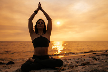 Fototapeta na wymiar A girl practices yoga by the sea during a beautiful sunset. Fitness and healthy lifestyle