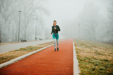 Photo of young sportive girl jogging outside on foggy morning.