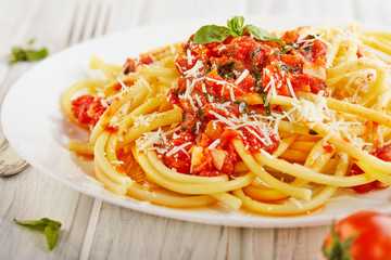 Tasty appetizing classic Italian spaghetti pasta with tomato sauce, parmesan and basil on a plate on a light wooden background. Side view. Copy space close-up