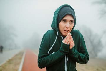 Close shot of young girl in warm sportswear trying to warm up her hands before starting with running session on cold day.