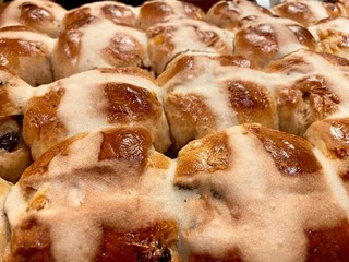 Front view of freshly baked, fruit-filled Hot Cross Buns, cooling on a rack. Traditional Good Friday / Easter baked goods. Shallow focus