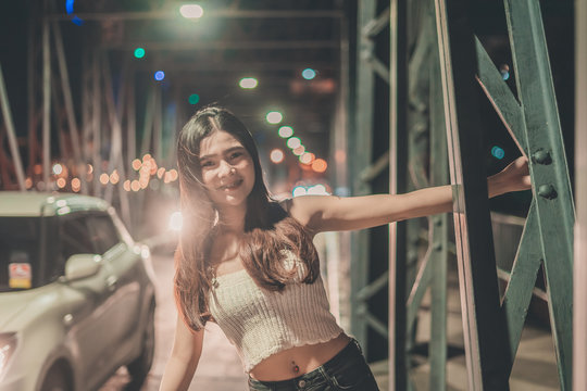 Portrait Of Smiling Young Woman Standing On Footbridge In City At Night